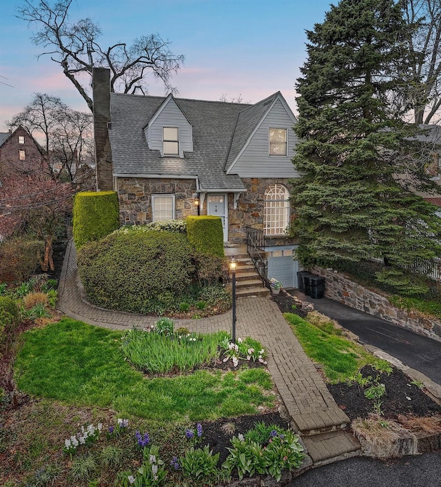 view of front of property with a chimney, stone siding, aphalt driveway, a garage, and a shingled roof
