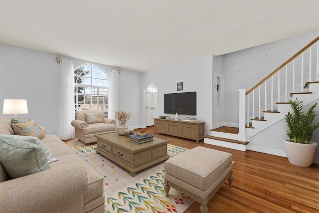 living area featuring arched walkways, stairs, light wood-type flooring, and baseboards