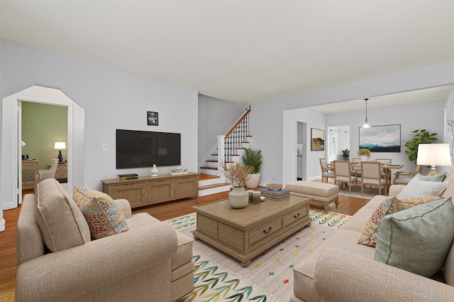 living room with baseboards, arched walkways, light wood-style floors, and stairs