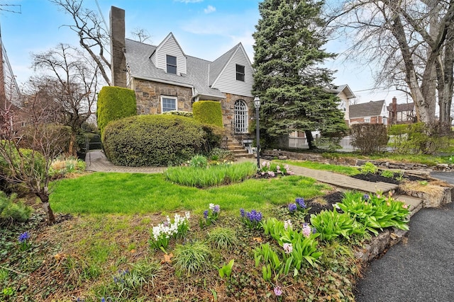 tudor home featuring a front yard, stone siding, and a chimney