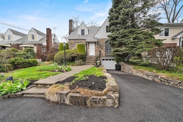 view of front of property featuring a garage, driveway, stone siding, and a chimney