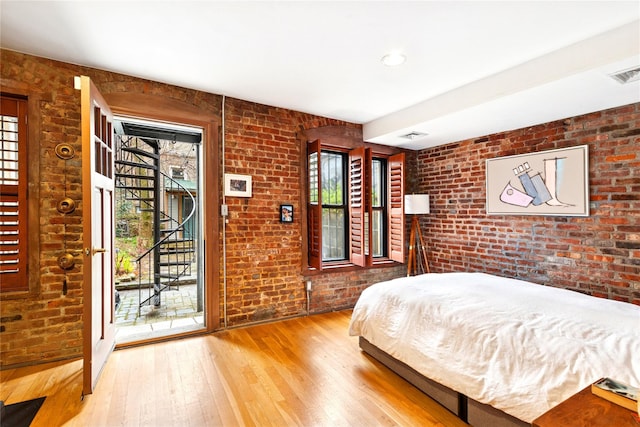 bedroom with brick wall, access to exterior, visible vents, and hardwood / wood-style flooring
