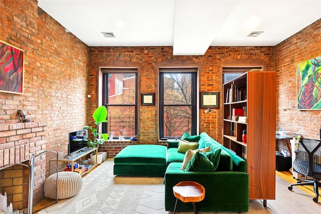 living area with visible vents, a brick fireplace, wood finished floors, and brick wall