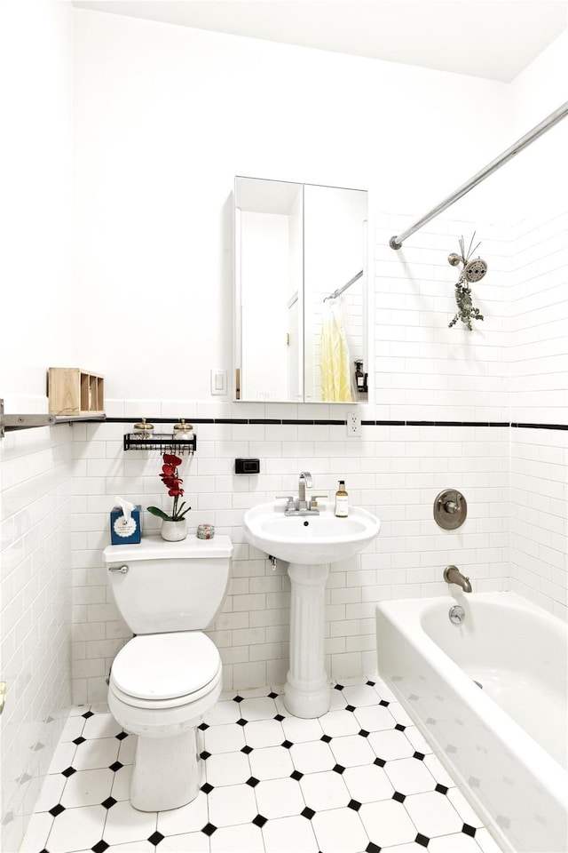 bathroom with bathing tub / shower combination, a wainscoted wall, toilet, tile walls, and a sink