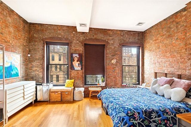 bedroom featuring brick wall, visible vents, and wood finished floors