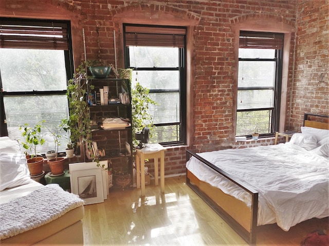 bedroom featuring brick wall, wood finished floors, and multiple windows