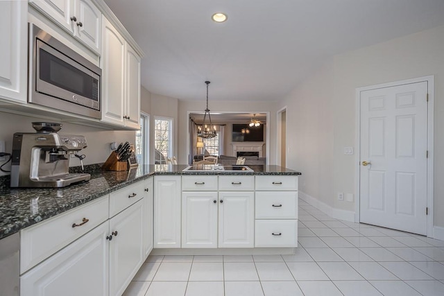 kitchen with dark stone countertops, white cabinets, a peninsula, stainless steel microwave, and light tile patterned flooring