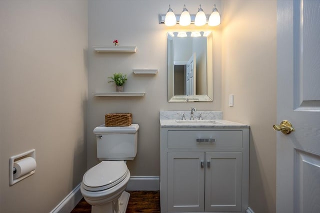 half bathroom with vanity, baseboards, toilet, and wood finished floors