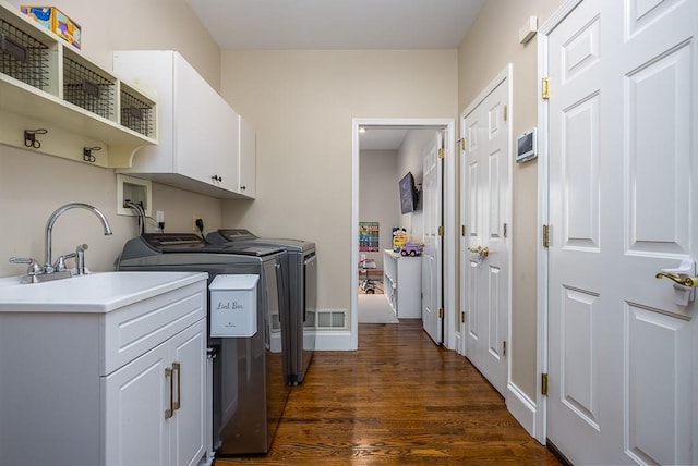 clothes washing area with a sink, washing machine and clothes dryer, cabinet space, and dark wood finished floors