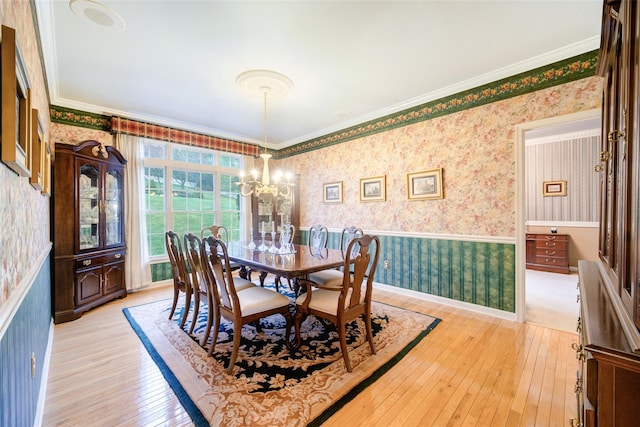 dining space featuring wallpapered walls, a wainscoted wall, light wood finished floors, crown molding, and a chandelier