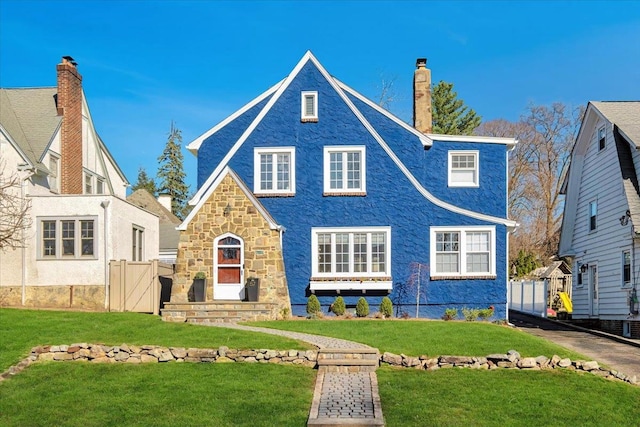 english style home featuring fence, a front lawn, and a chimney