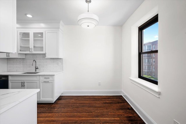 kitchen featuring a sink, baseboards, tasteful backsplash, dark wood-style floors, and glass insert cabinets