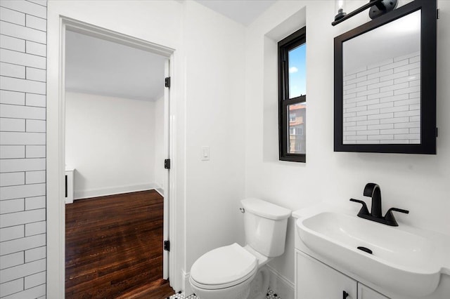 bathroom featuring baseboards, wood finished floors, toilet, and vanity