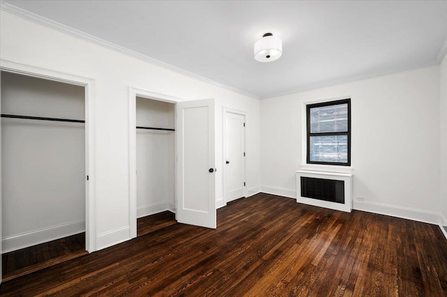 unfurnished bedroom featuring baseboards, multiple closets, crown molding, and hardwood / wood-style floors
