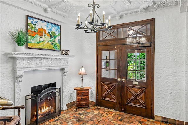 interior space featuring a textured wall, brick patterned floor, baseboards, a lit fireplace, and a notable chandelier