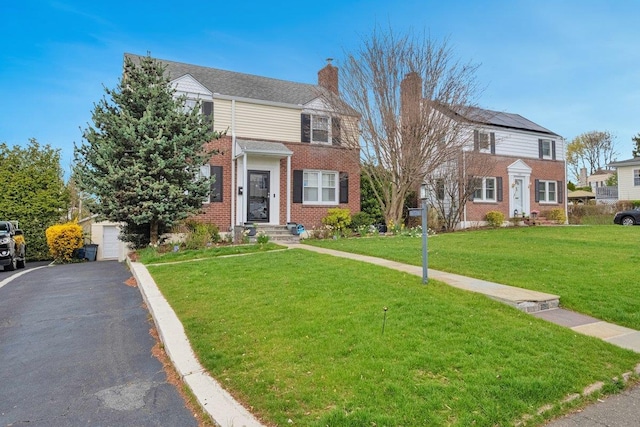 view of front of house with aphalt driveway, a chimney, a front yard, and brick siding