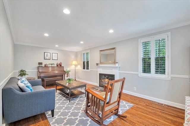 living room featuring recessed lighting, light wood-type flooring, a glass covered fireplace, visible vents, and crown molding