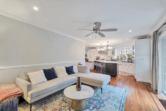 living room featuring crown molding, light wood-style flooring, recessed lighting, and ceiling fan with notable chandelier