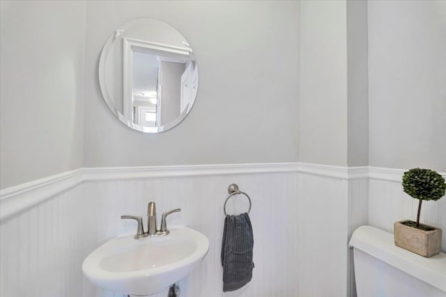 half bath with wainscoting, toilet, and a sink