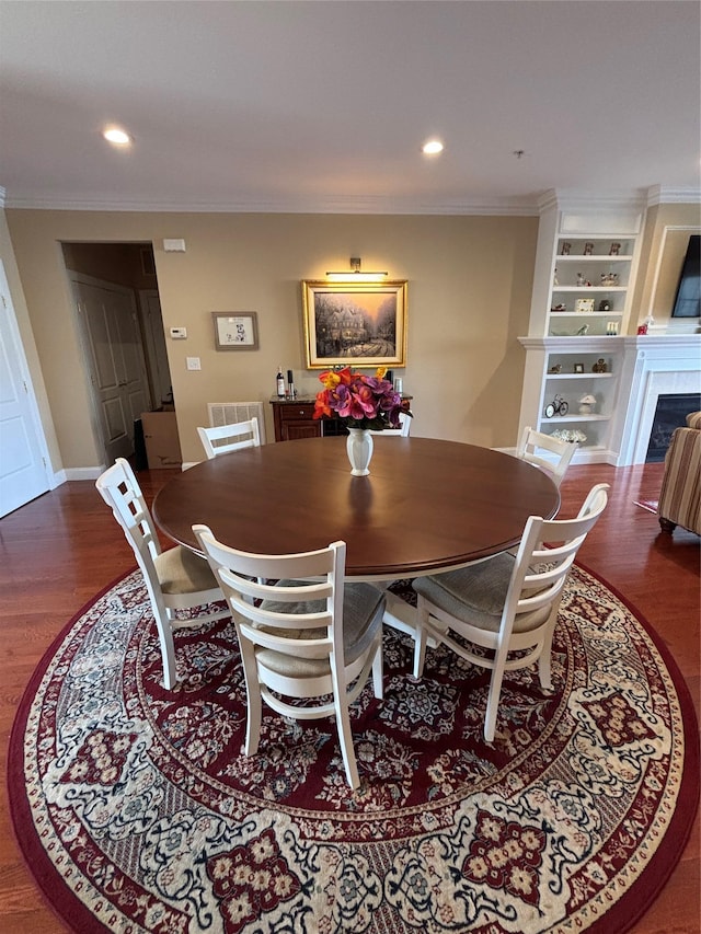 dining area featuring a tiled fireplace, ornamental molding, built in features, and dark wood finished floors