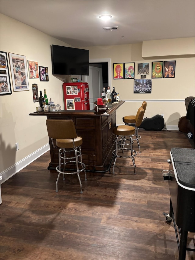 bar with a bar, wood finished floors, baseboards, and visible vents