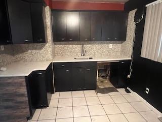 kitchen with dark cabinets, tasteful backsplash, light countertops, light tile patterned flooring, and a sink