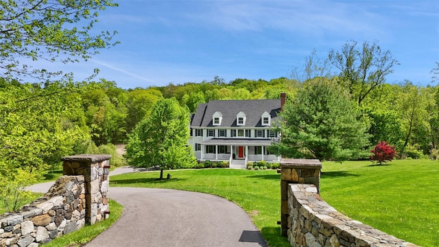 view of front of home featuring a chimney, a porch, a front lawn, and a view of trees