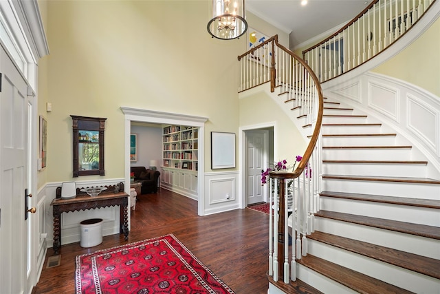 foyer featuring a towering ceiling, wood finished floors, stairs, a chandelier, and a wainscoted wall