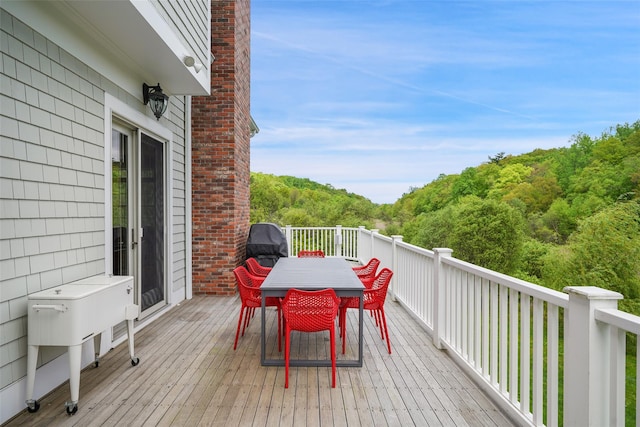 wooden terrace featuring outdoor dining area and a wooded view
