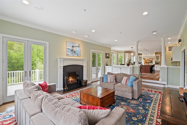 living room with wood finished floors, a warm lit fireplace, french doors, recessed lighting, and crown molding
