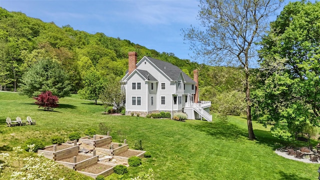 back of property featuring a chimney, a lawn, a vegetable garden, and a forest view