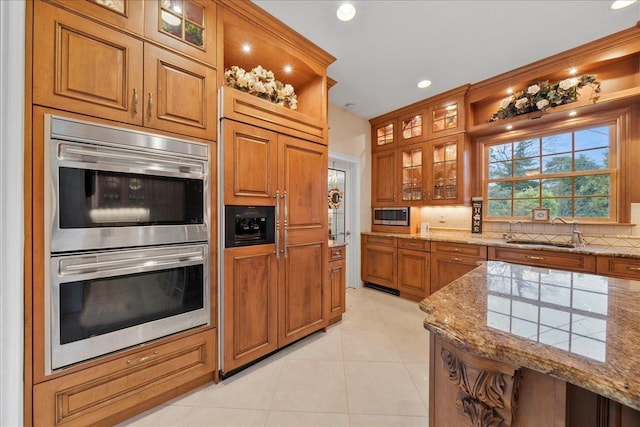 kitchen featuring a sink, brown cabinets, decorative backsplash, light tile patterned floors, and built in appliances