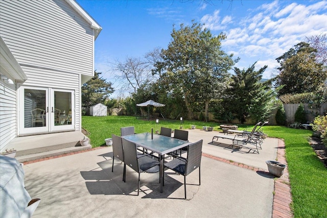 view of patio featuring a storage unit, french doors, a fenced backyard, an outdoor structure, and outdoor dining space