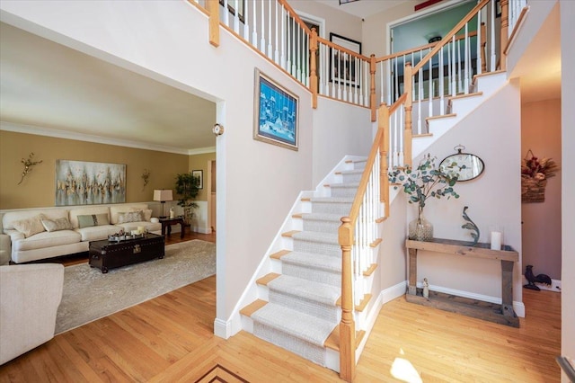 stairs featuring baseboards, ornamental molding, a towering ceiling, and wood finished floors