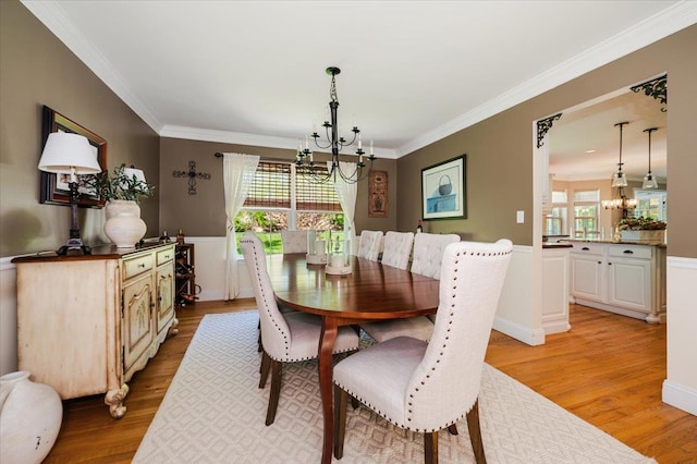 dining space with an inviting chandelier, crown molding, wainscoting, and light wood-style flooring