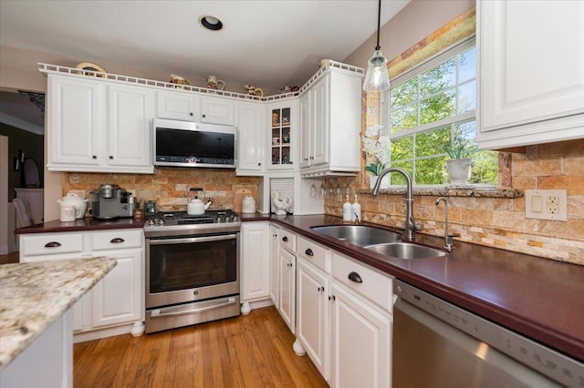kitchen with a sink, stainless steel appliances, decorative light fixtures, white cabinetry, and tasteful backsplash
