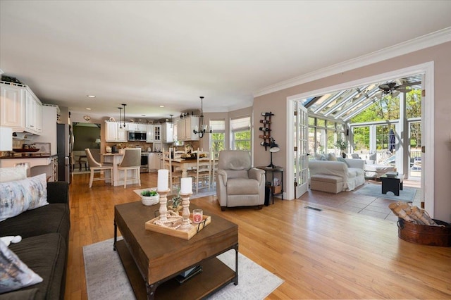 living room with ceiling fan, ornamental molding, light wood-style flooring, and visible vents