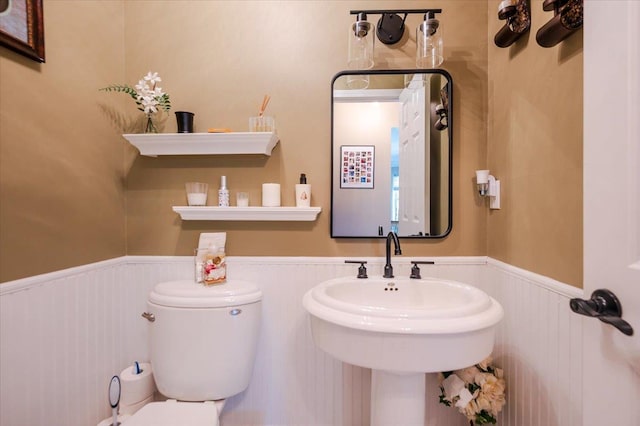 half bath featuring a wainscoted wall and toilet