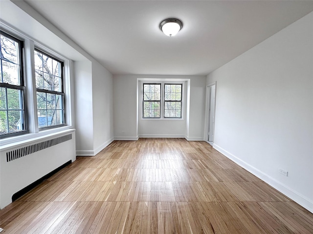 spare room featuring wood finished floors, baseboards, and radiator heating unit