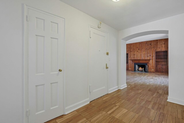 hall featuring arched walkways, baseboards, and wood walls