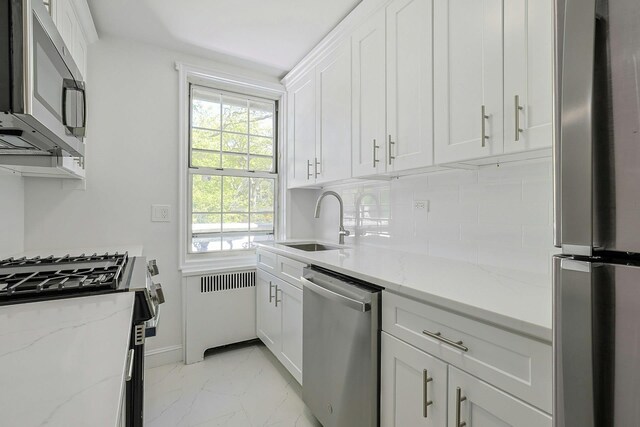 kitchen with white cabinets, appliances with stainless steel finishes, a sink, marble finish floor, and tasteful backsplash