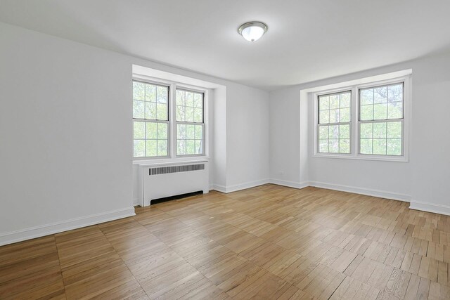 empty room featuring baseboards, radiator heating unit, and wood finished floors