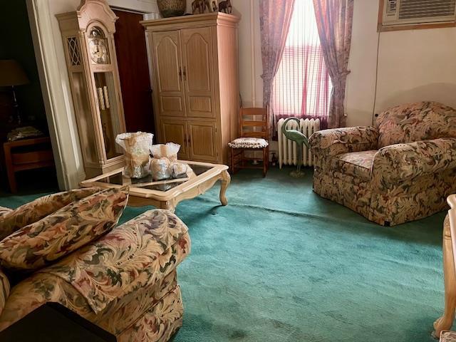 living area with radiator heating unit, carpet, and a wall mounted air conditioner