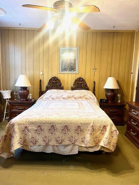 bedroom with wood walls, a ceiling fan, and carpet floors