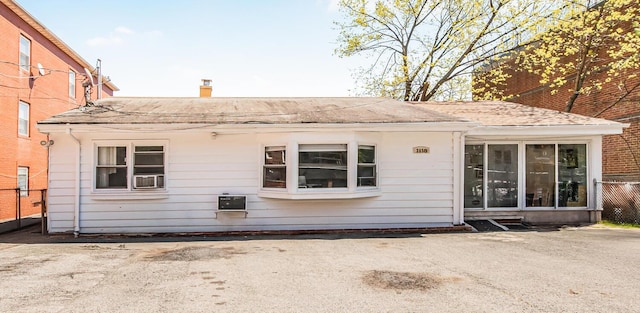 back of property with a chimney, roof with shingles, and fence