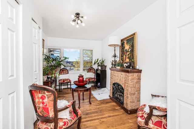 living area featuring baseboard heating, an inviting chandelier, wood finished floors, and a fireplace