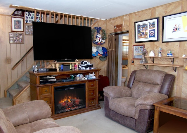 living room featuring wooden walls, stairs, carpet floors, and a glass covered fireplace