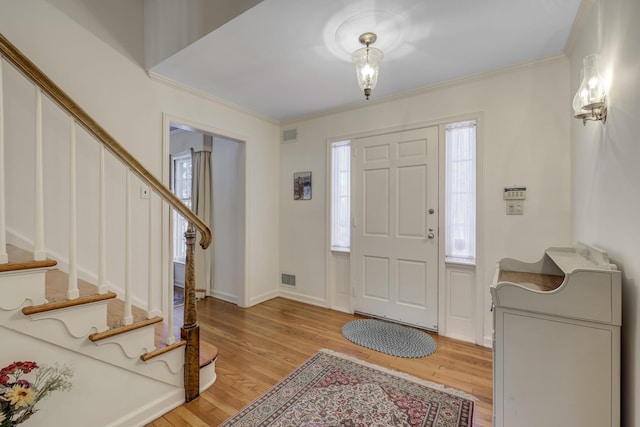 foyer entrance with light wood-style floors, crown molding, visible vents, and stairway
