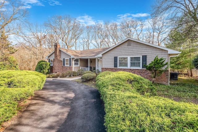 ranch-style home with a porch, a chimney, aphalt driveway, and brick siding