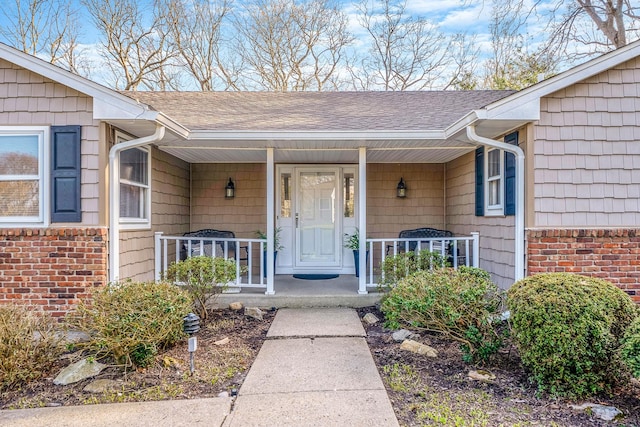 view of exterior entry with a porch and a shingled roof
